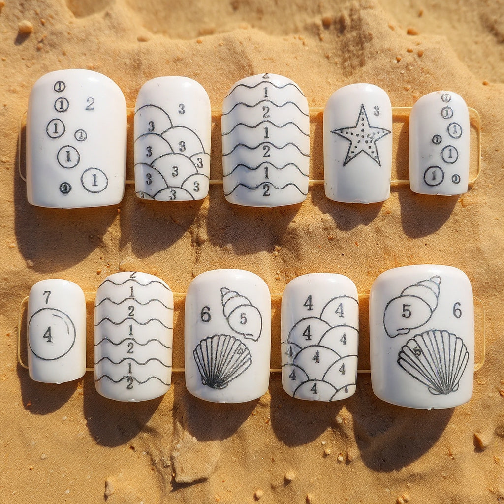Set of white nail wraps with black designs on a sandy background